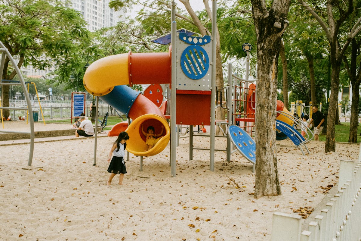 Children playing at a sunny Barcelona park playground surrounded by palm trees