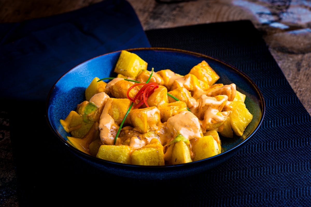 Golden patatas bravas topped with spicy red sauce and aioli in a traditional ceramic dish