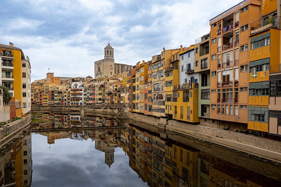 The colourful houses of Girona reflected in the Onyar river under a footbridge