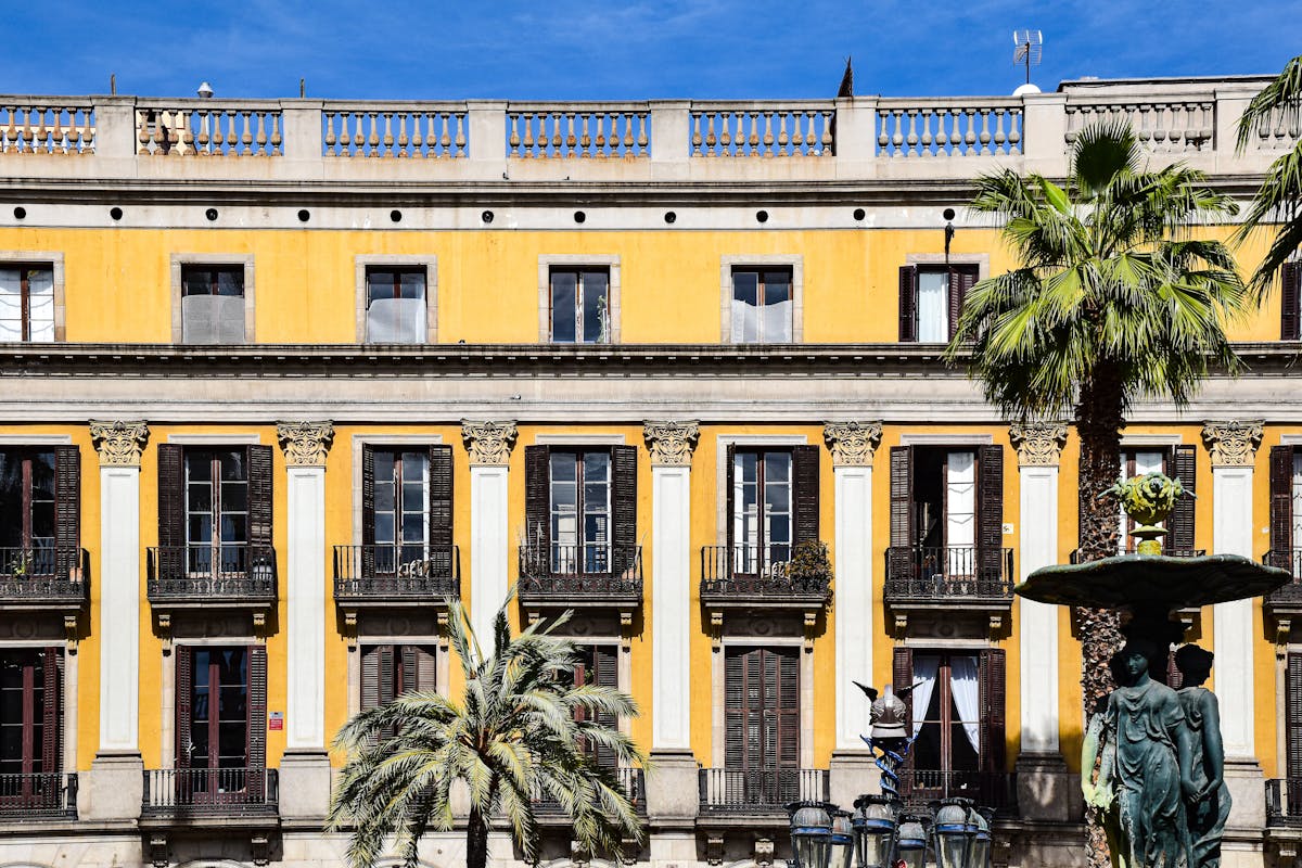 Placa Reial in the Gothic Quarter Barcelona with palm trees, arcaded buildings, and Gaudi lampposts