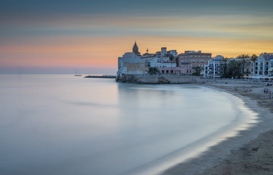 A Sitges beach with sunbathers, the church on the headland, and the Mediterranean stretching to the horizon