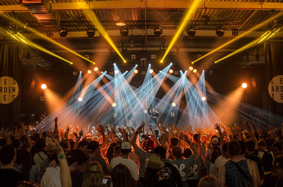 A festival crowd watching a stage with bright lights and pyrotechnics