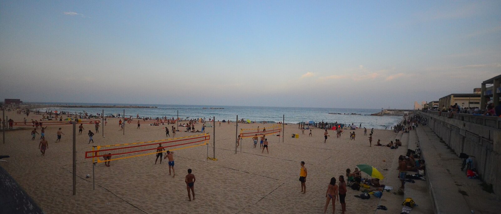 A Barcelona beach on a summer evening, with people playing volleyball on the sand and swimmers in the sea