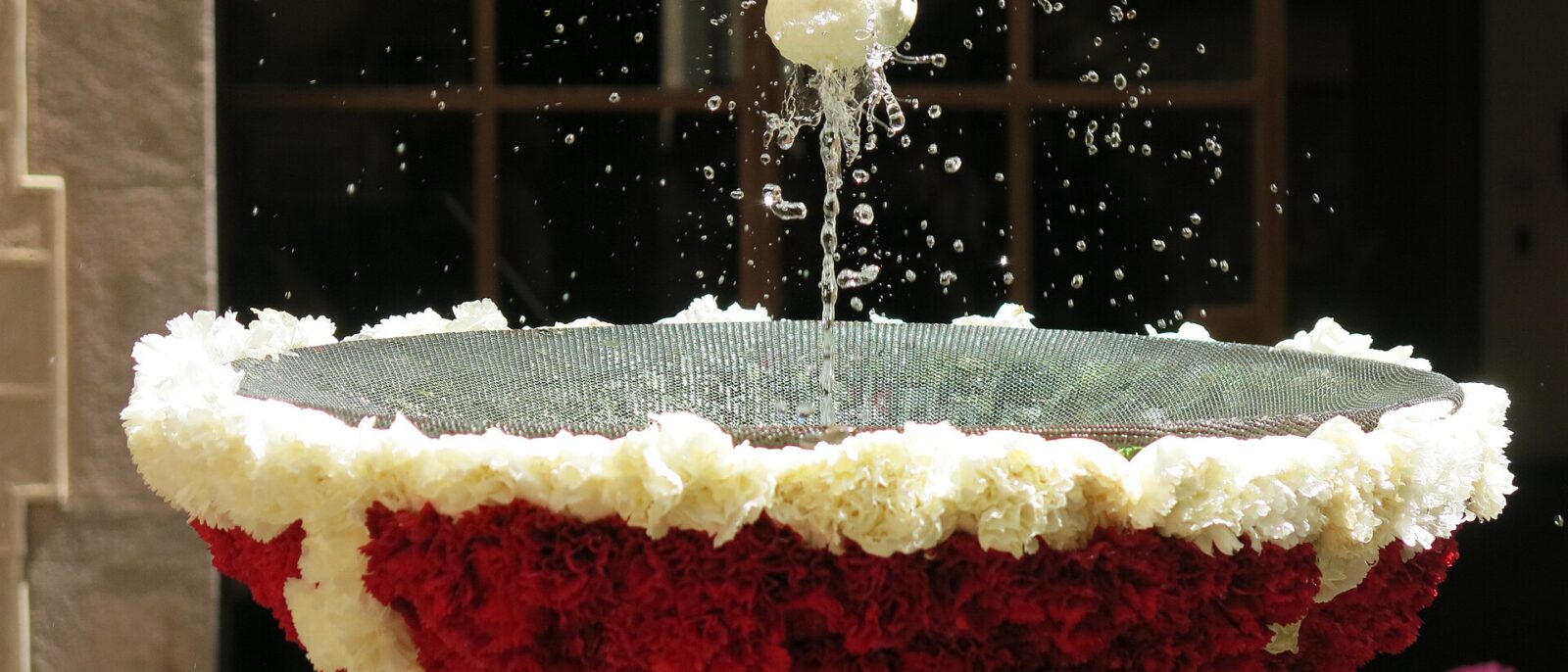 An eggshell dancing on a jet of water above a fountain decorated with red and white carnations for l'Ou com balla in Barcelona