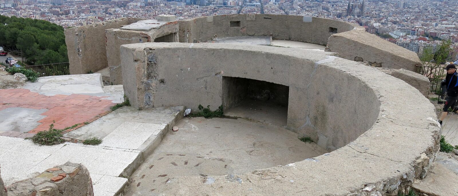 A circular concrete gun emplacement on the Turo de la Rovira with the Barcelona skyline, the Sagrada Familia and the sea beyond