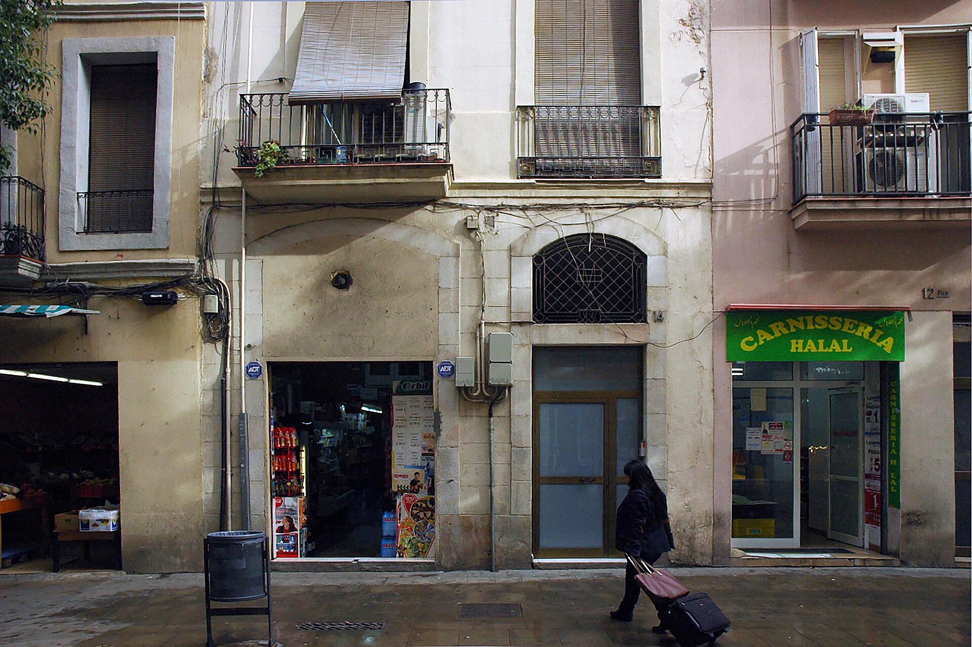 A woman wheeling a suitcase past local shops on Carrer Blai in Poble Sec, Barcelona