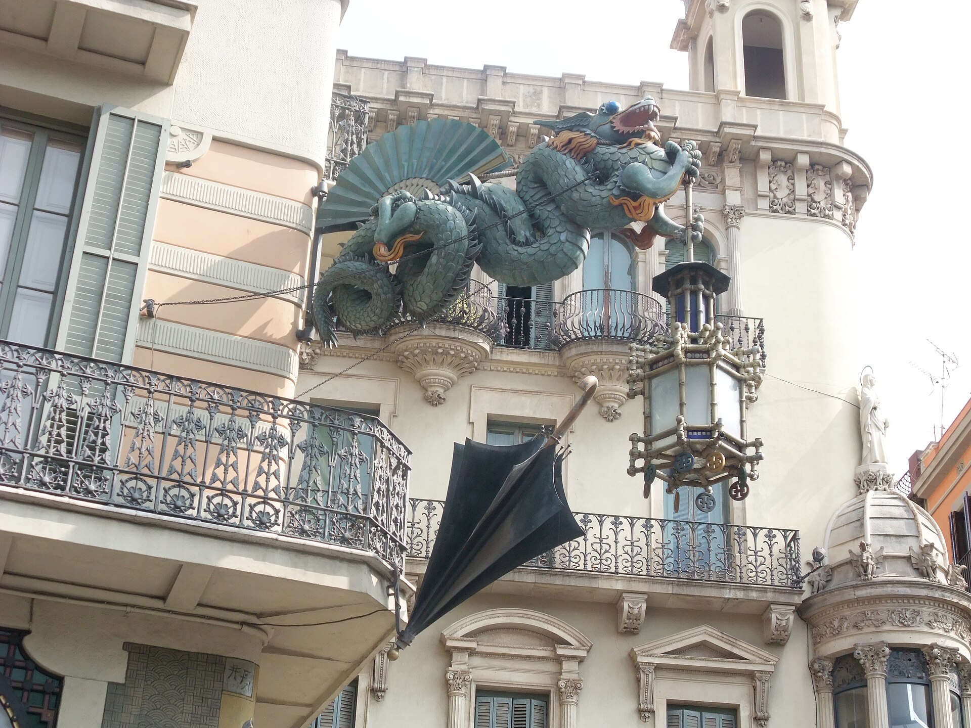 A green Chinese dragon holding a lantern above an umbrella on the facade of Casa Bruno Cuadros on La Rambla