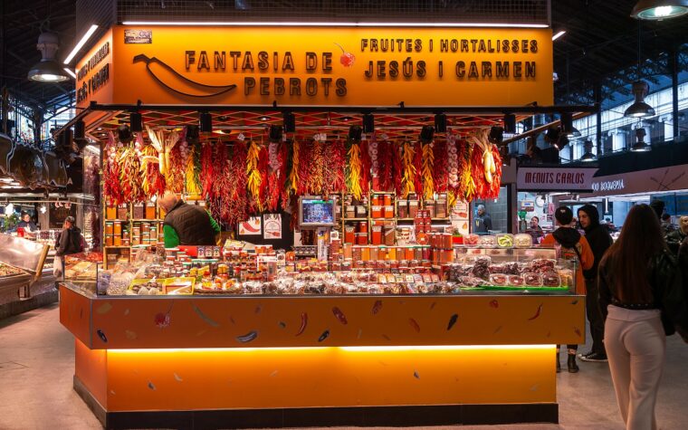A brightly lit stall in La Boqueria market hung with strings of red and yellow chillies, garlic and jars of spices