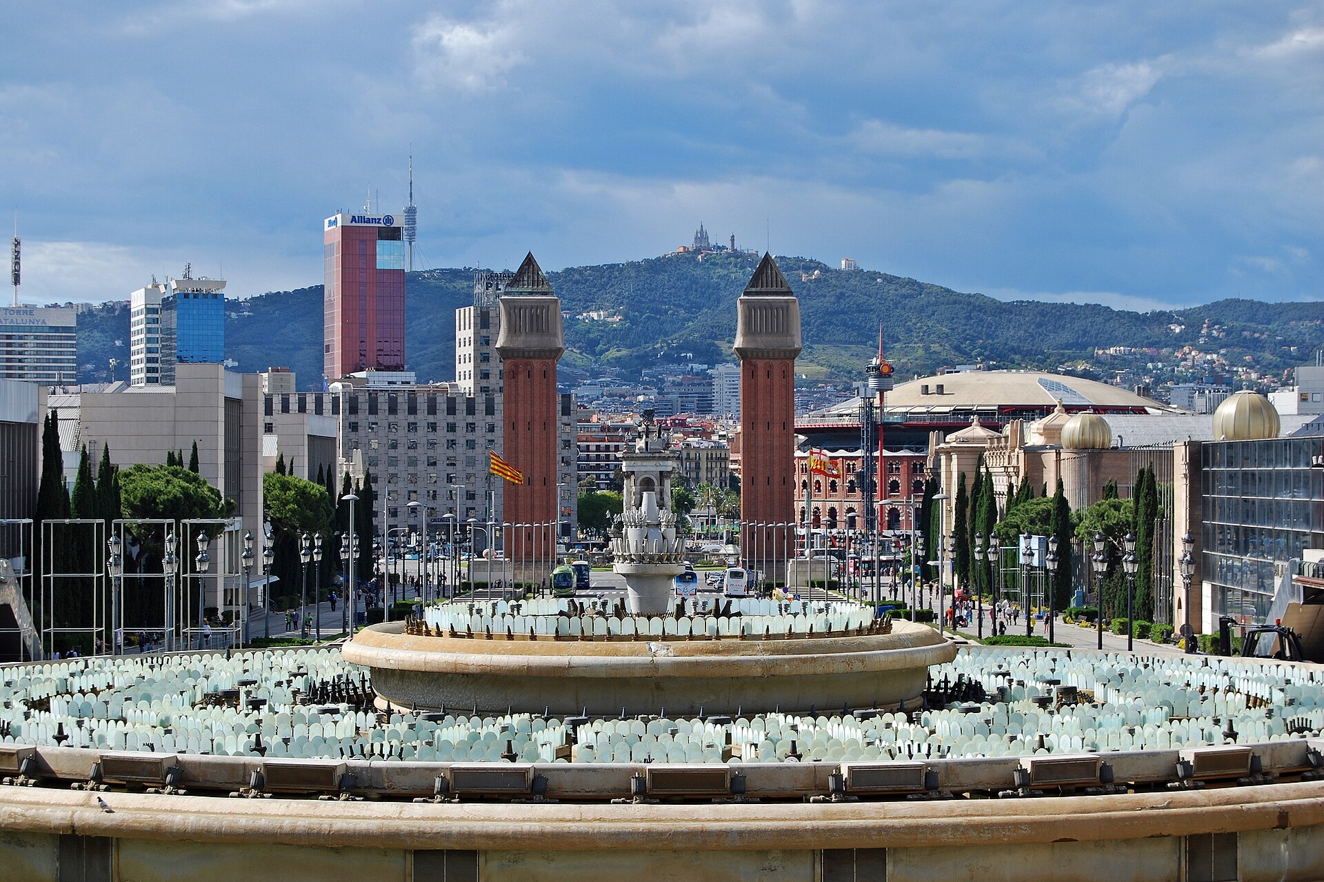 Close view of the Magic Fountain's rings of nozzles and lamps in daylight, with the Venetian towers and Tibidabo beyond