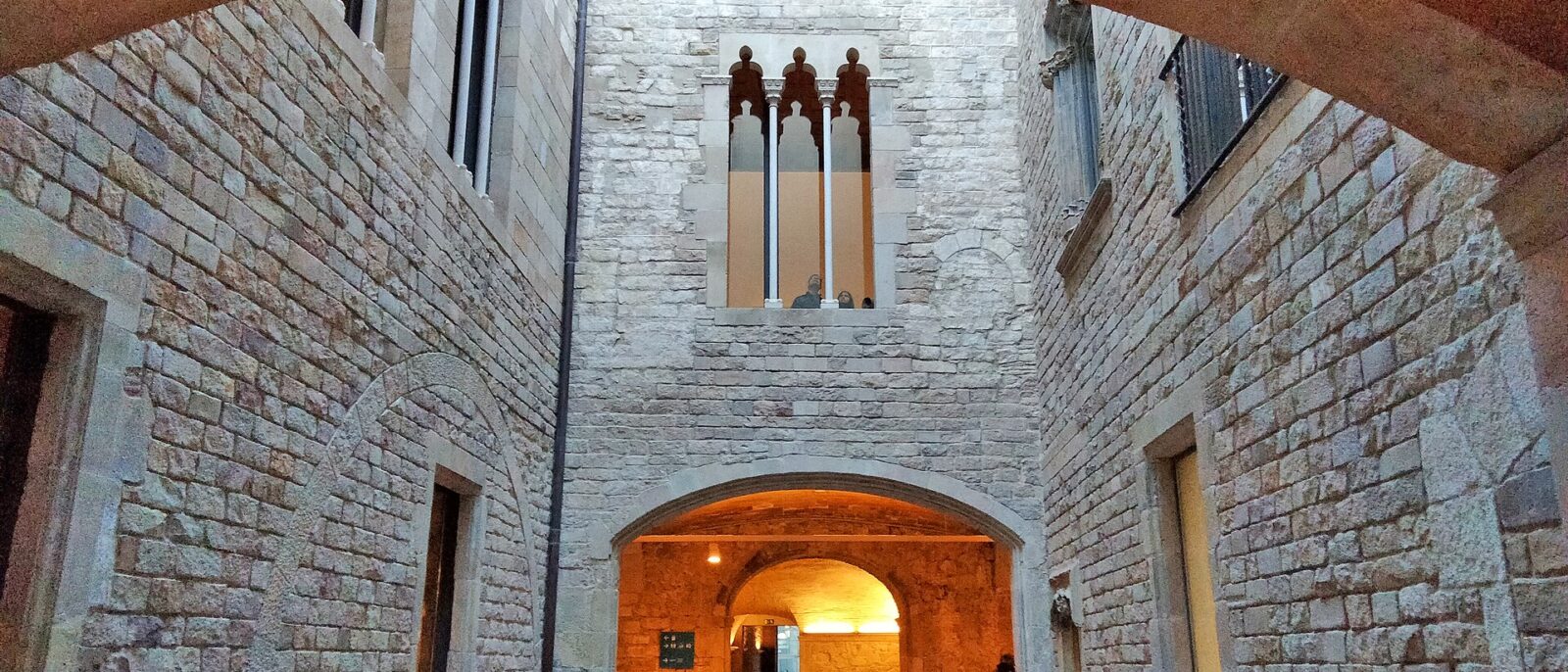 Stone courtyard of the Palau del Baro de Castellet at the Picasso Museum, with a Gothic triple window and a lit archway