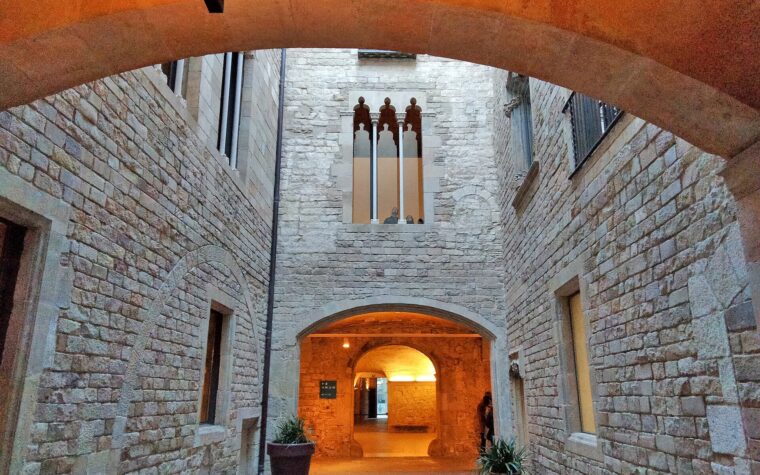 Stone courtyard of the Palau del Baro de Castellet at the Picasso Museum, with a Gothic triple window and a lit archway