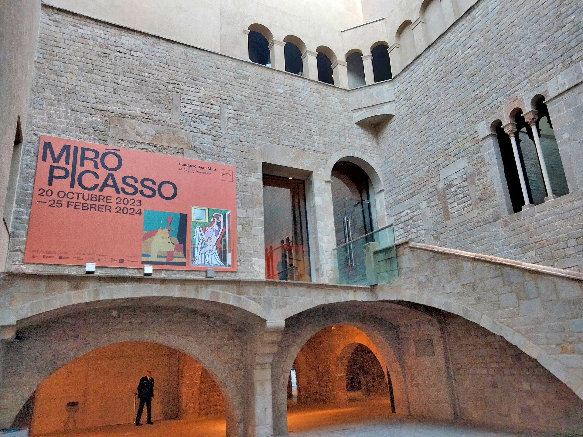 The stone courtyard of the Palau Finestres at the Picasso Museum, with arched galleries, an external staircase and an exhibition banner