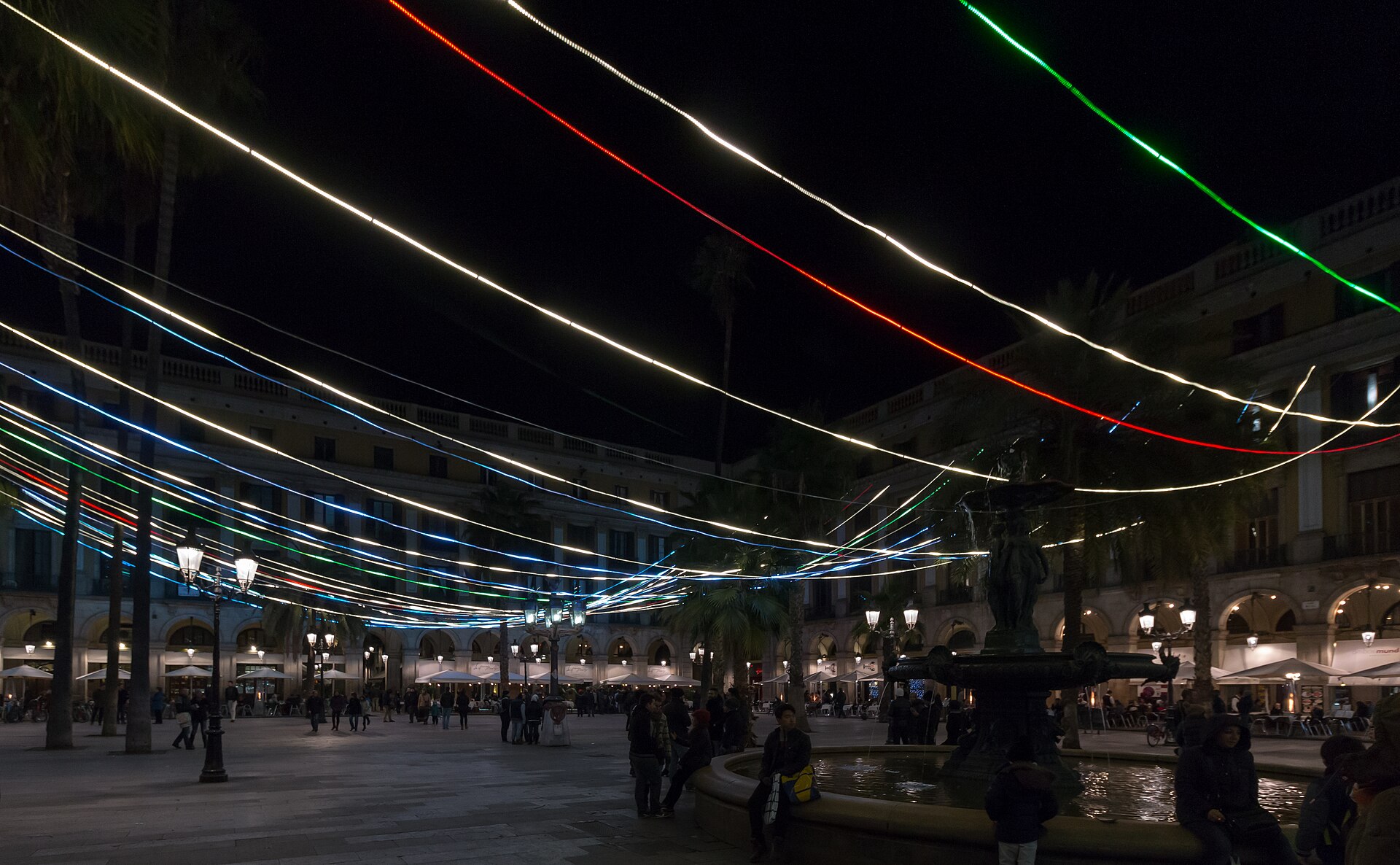 Plaça Reial in Barcelona at night, lit with strings of coloured lights above the fountain