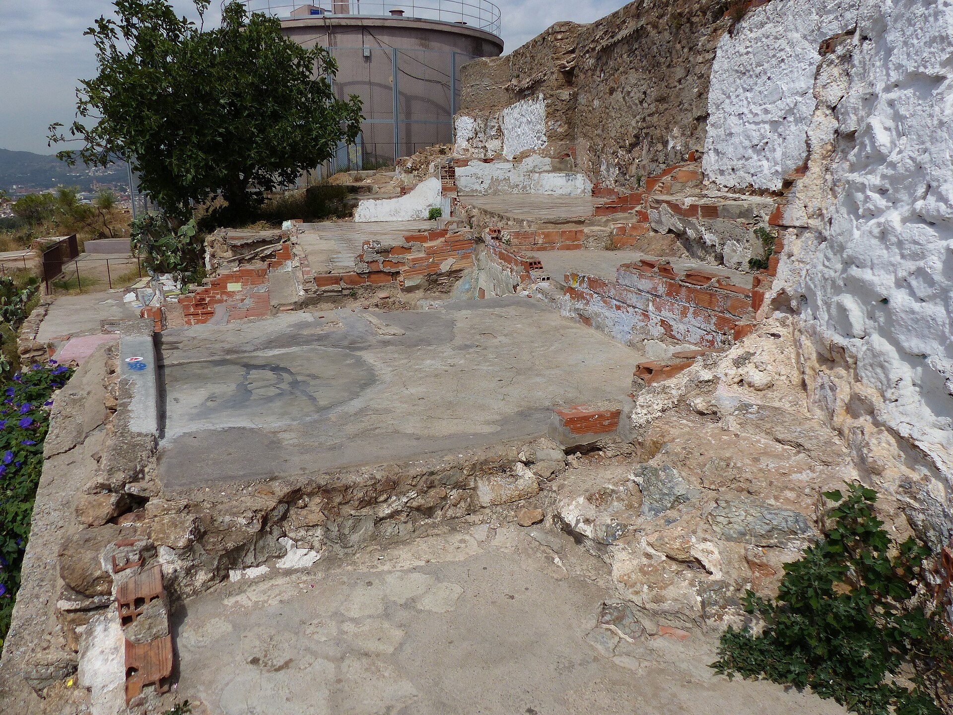 Remains of brick and whitewashed shack walls built into the old gun battery on the Turo de la Rovira, with a water tank behind