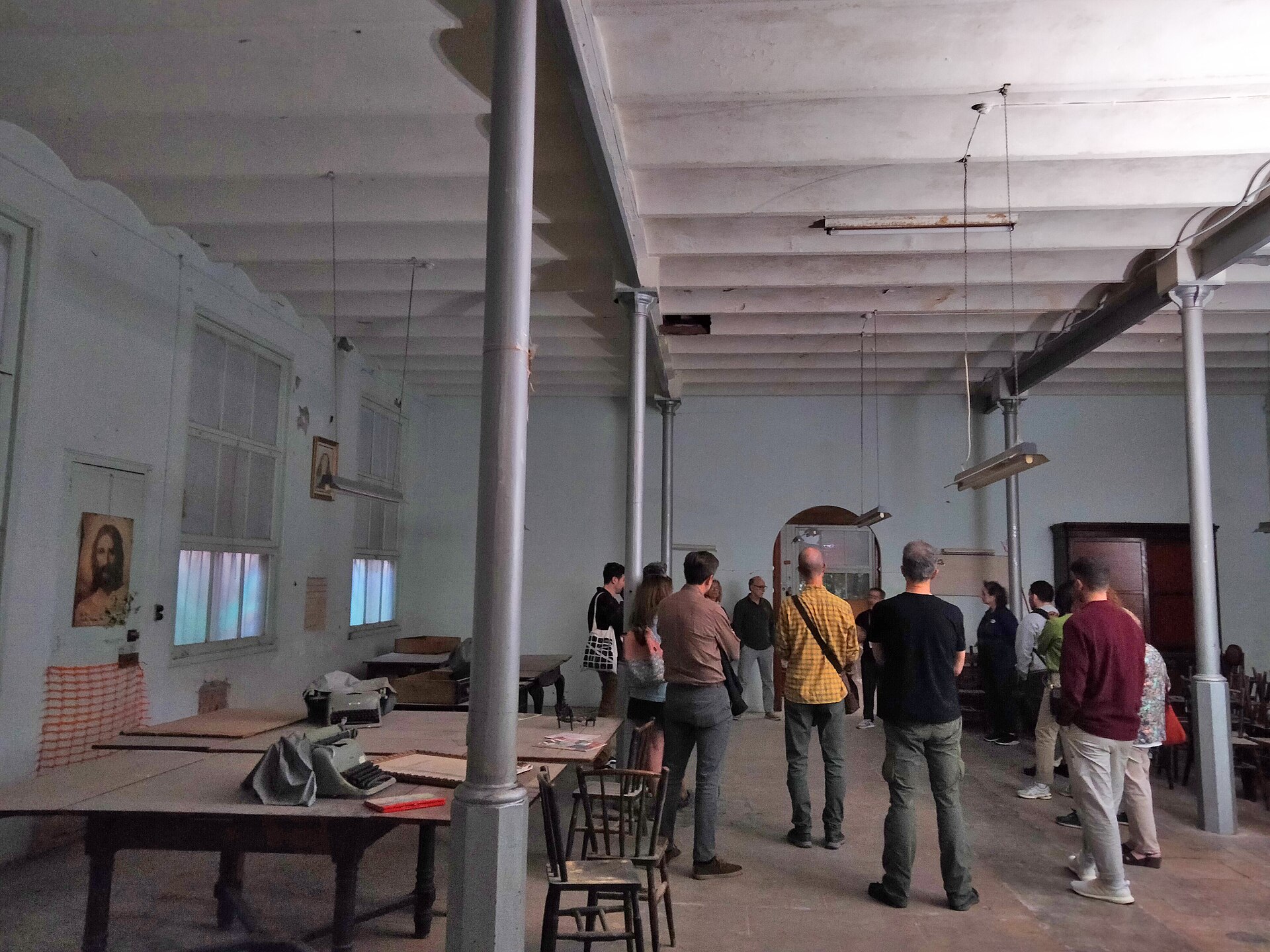 Visitors on a guided tour of an old workshop with iron columns, long tables and a typewriter, during 48h Open House BCN