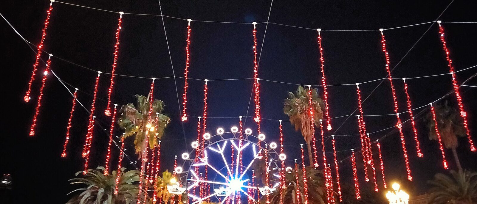 Strings of red Christmas lights hung between palm trees on the Moll de la Fusta, with an illuminated Ferris wheel and crowds below