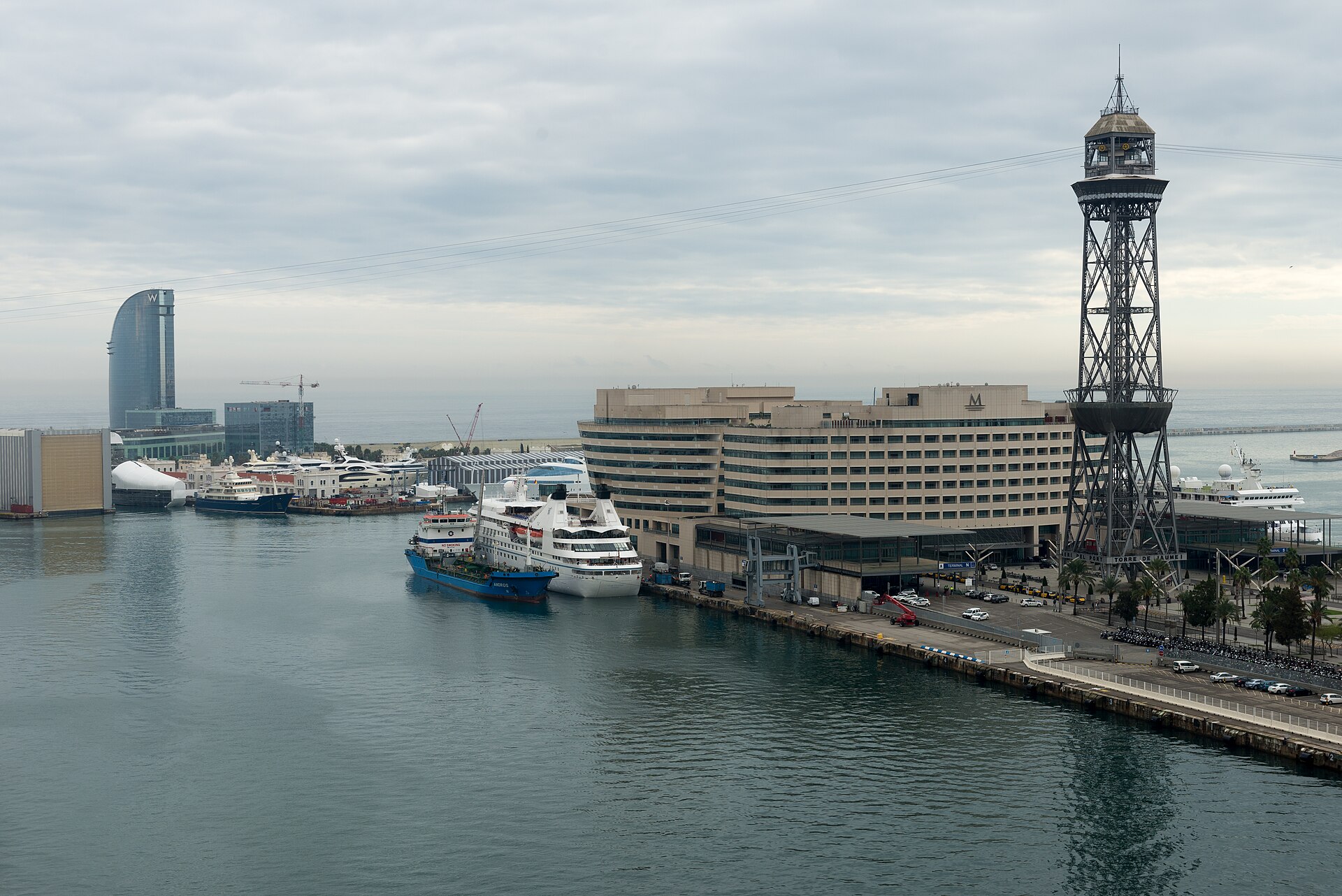 A small cruise ship berthed at the World Trade Center terminal in Barcelona's old port, with the steel tower of the port cable car on the right