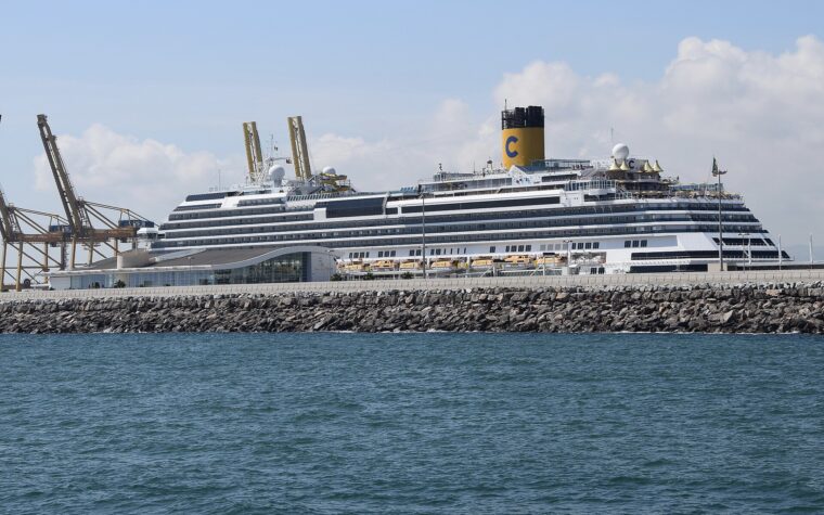 A Costa cruise ship berthed beside a terminal building on the Moll Adossat in Barcelona, with container cranes on the left