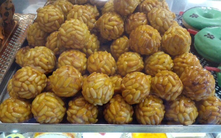 A tray of pine-nut panellets in a pastry shop window, with Halloween-decorated doughnuts beside them