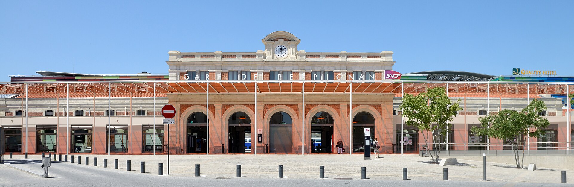 The red-brick and stone facade of Perpignan railway station, with a clock above the entrance arches