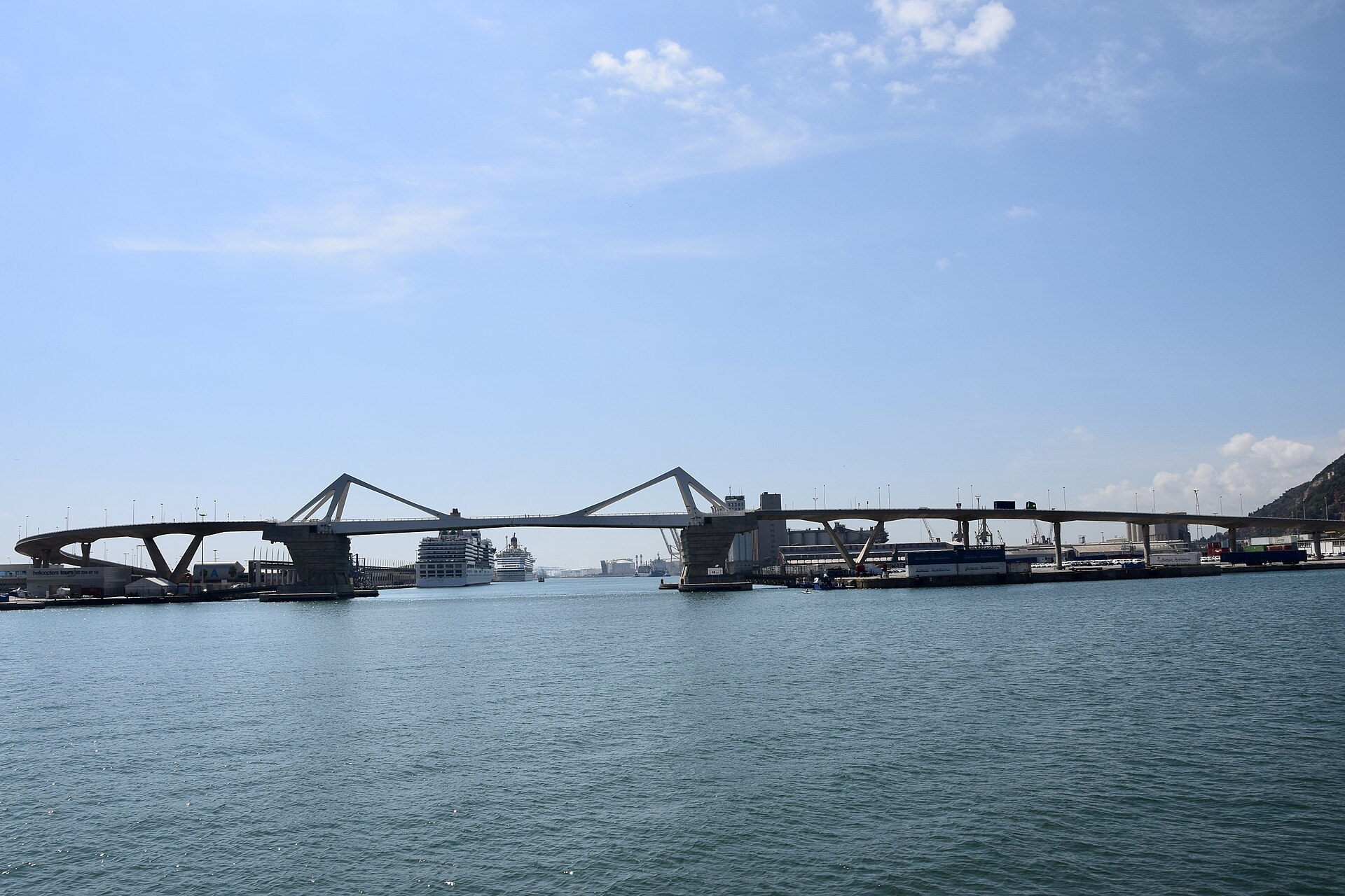 The white Porta d'Europa drawbridge spanning Barcelona's port, with two cruise ships berthed beyond it