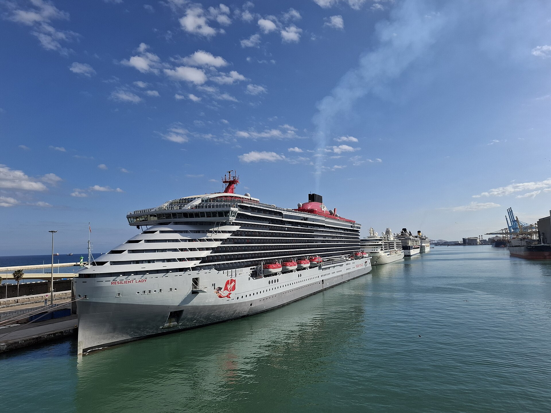 The Virgin Voyages ship Resilient Lady berthed at the Moll Adossat in Barcelona, with several more cruise ships lined up behind it
