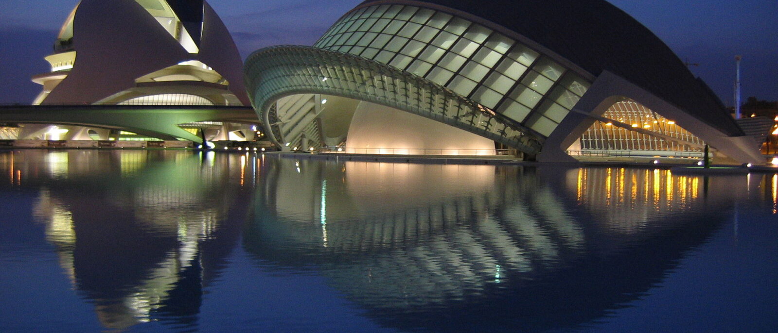 The Hemisferic and the Palau de les Arts at the City of Arts and Sciences in Valencia, lit up at dusk and reflected in a pool
