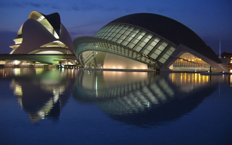 The Hemisferic and the Palau de les Arts at the City of Arts and Sciences in Valencia, lit up at dusk and reflected in a pool